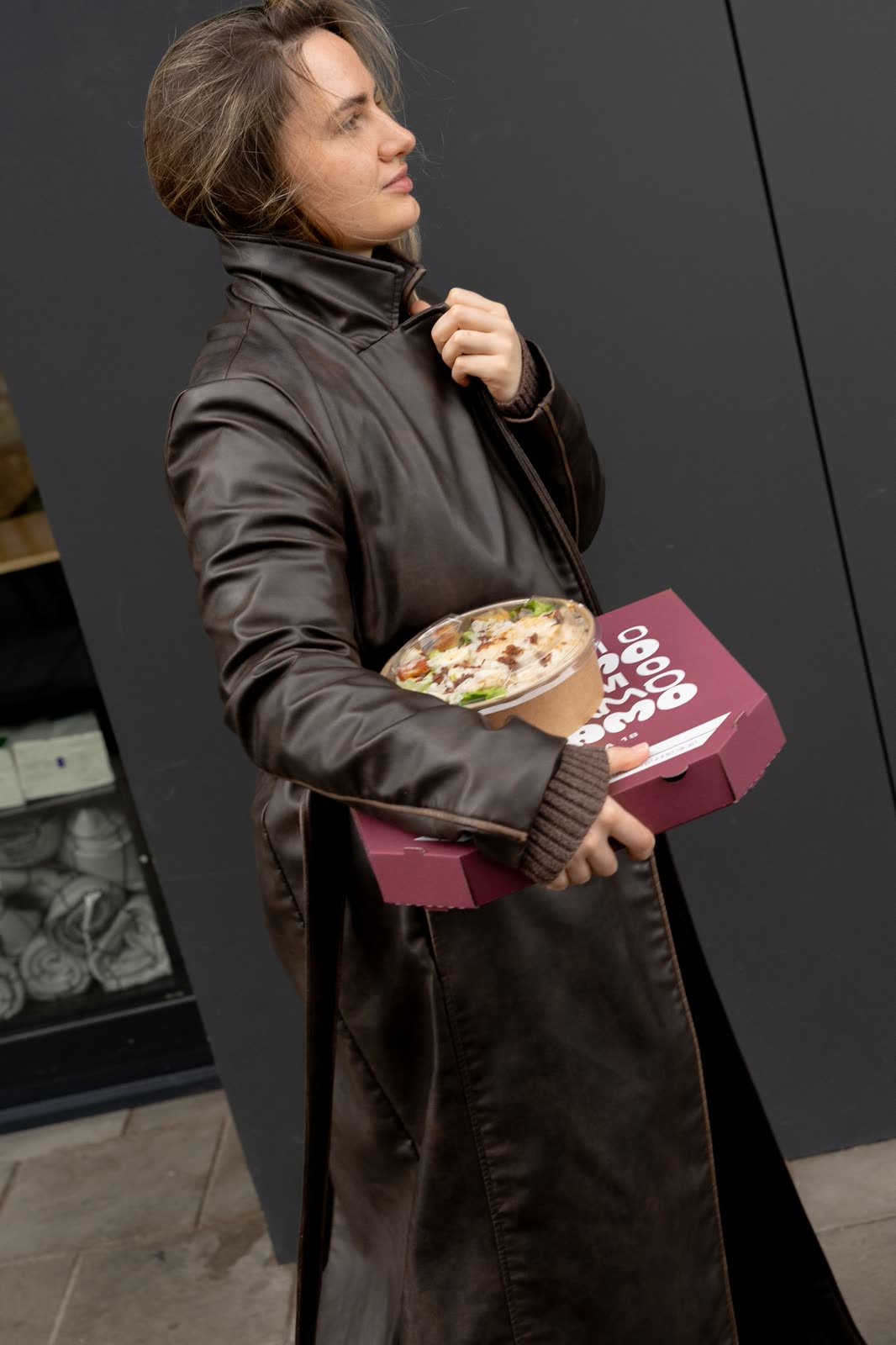 Guest in a leather coat carrying a pizza box